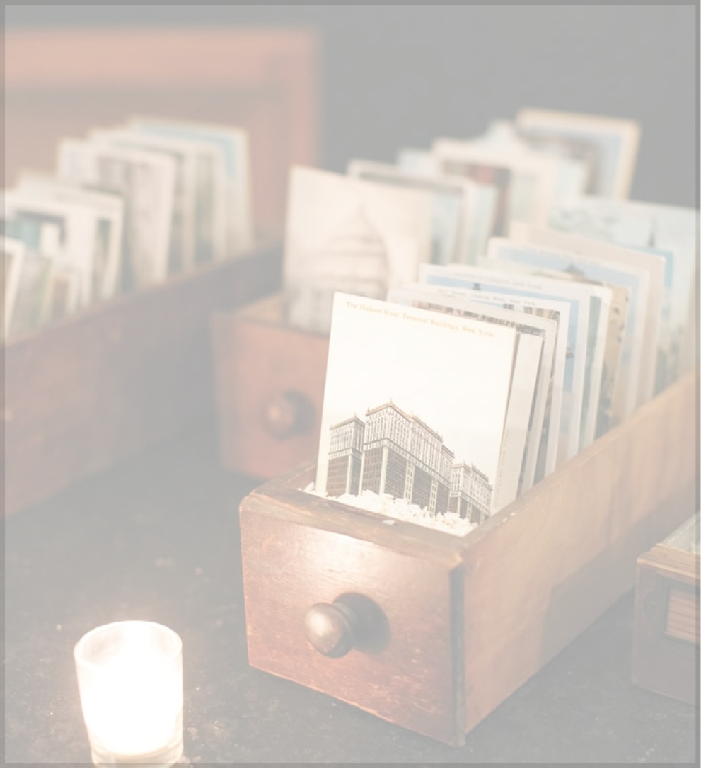 Vintage postcards in wooden box, candle nearby.